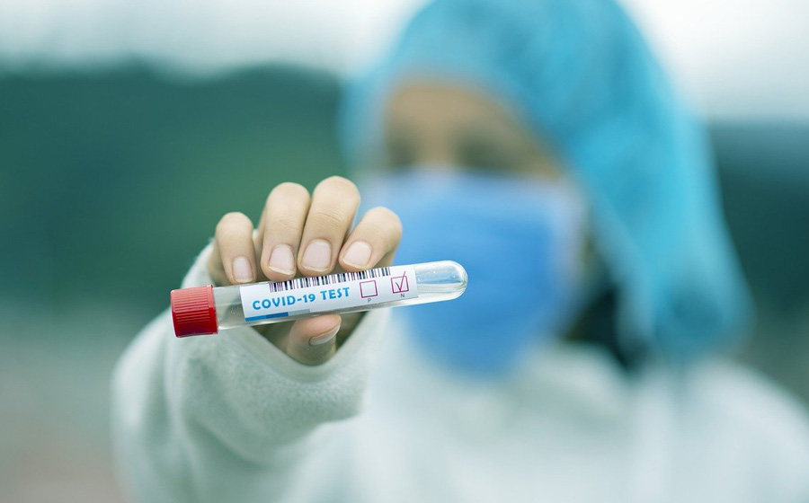 Photo of a Covid-19 test tube held by a masked medic.