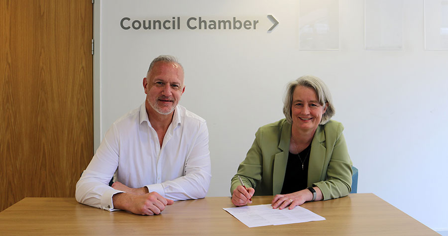 Cllr Ian Boulton (Labour group leader) and Cllr Claire Young (Liberal Democrat leader) sign an agreement to form an administration to run South Gloucestershire Council. Photo of two people seated at a table and signing an agreement.