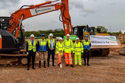 Photo of a group of people in hard hats standing in front of an excavator.