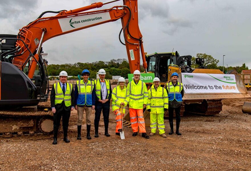 Photo of a group of people in hard hats standing in front of an excavator.