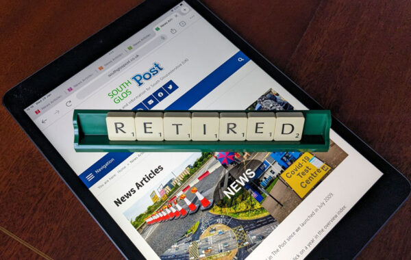Photo of letter tiles spelling the word 'Retired' in a rack placed over a webpage displayed on an iPad.
